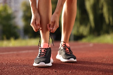 Photo of Woman tying shoelace of sneaker at stadium, closeup