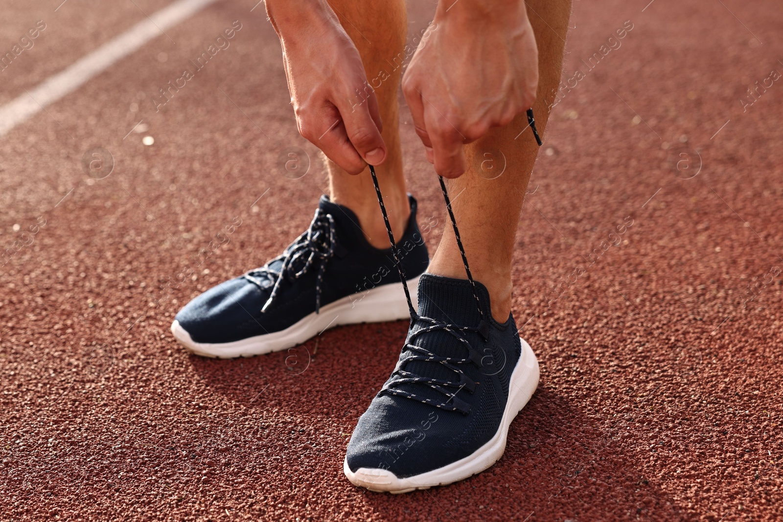 Photo of Man tying shoelace of black sneaker at stadium, closeup