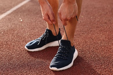 Man tying shoelace of black sneaker at stadium, closeup