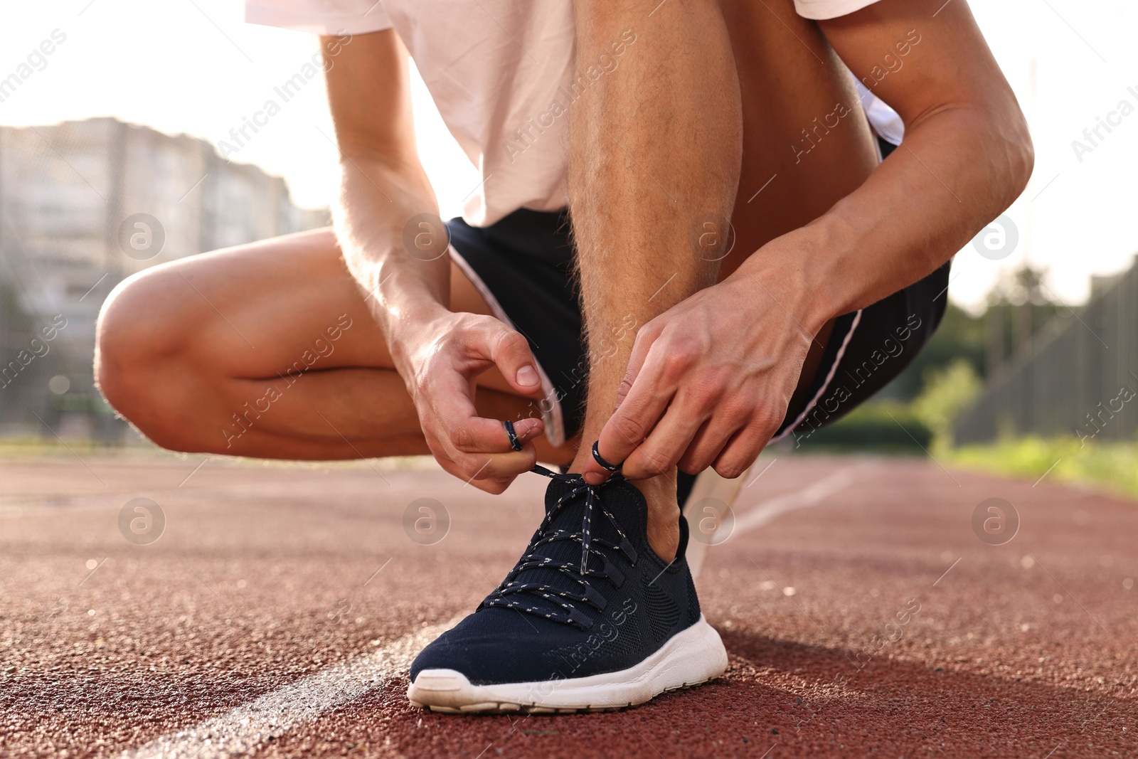 Photo of Man tying shoelace of black sneaker at stadium, closeup