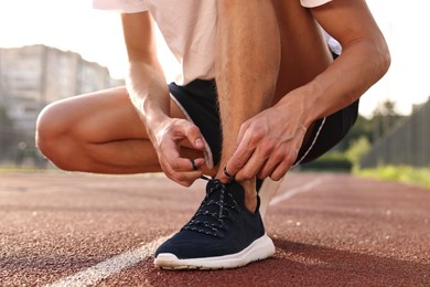 Photo of Man tying shoelace of black sneaker at stadium, closeup