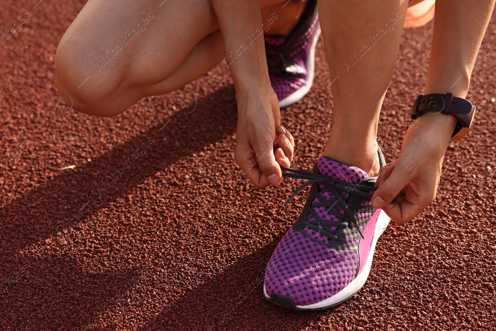 Photo of Woman tying shoelace of sneaker at stadium, closeup