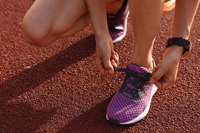 Photo of Woman tying shoelace of sneaker at stadium, closeup