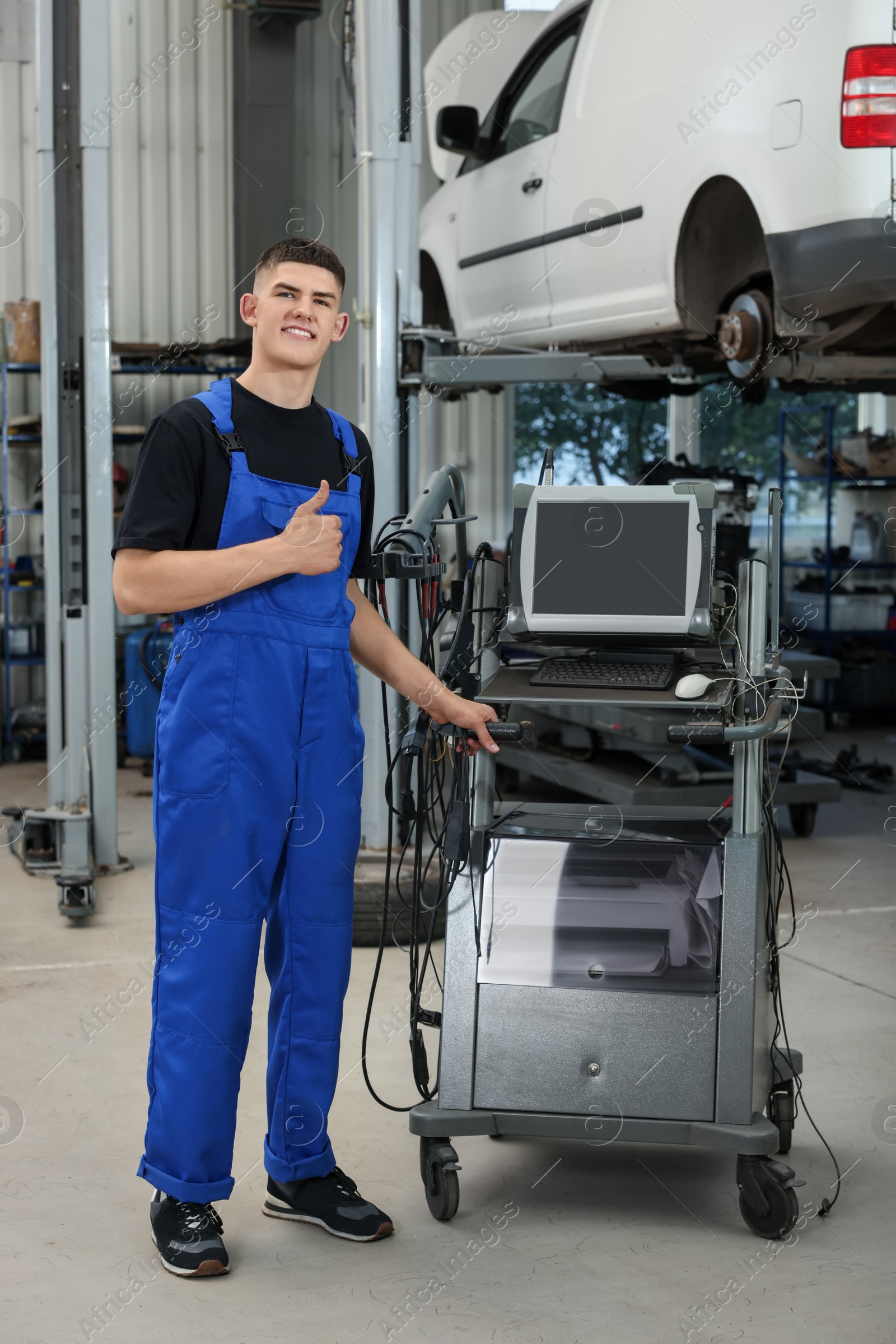 Photo of Young auto mechanic showing thumbs up at automobile repair shop