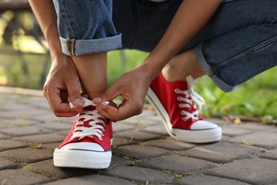 Photo of Woman tying shoelace of red sneaker outdoors, closeup