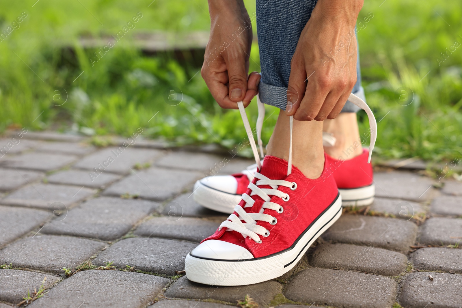 Photo of Woman tying shoelace of red sneaker outdoors, closeup. Space for text