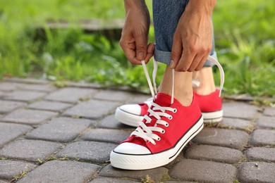 Photo of Woman tying shoelace of red sneaker outdoors, closeup. Space for text