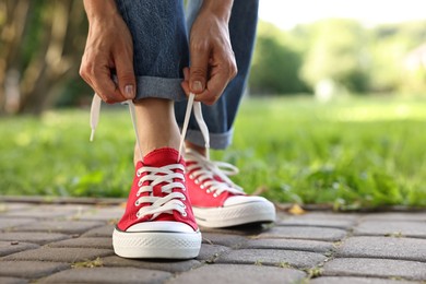 Photo of Woman tying shoelace of red sneaker outdoors, closeup. Space for text