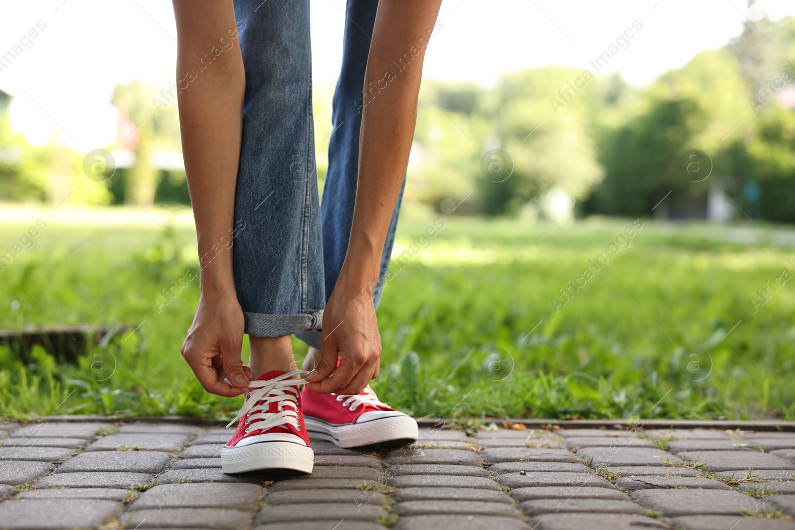 Photo of Woman tying shoelace of red sneaker outdoors, closeup. Space for text