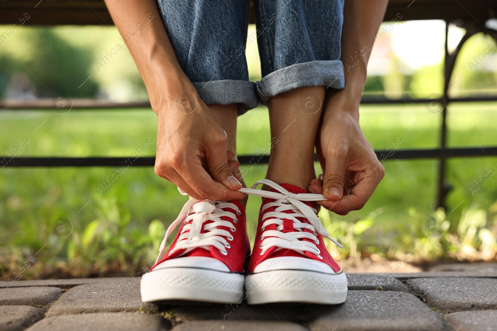 Photo of Woman tying shoelace of red sneaker outdoors, closeup