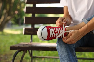 Photo of Woman tying shoelace of red sneaker on bench outdoors, closeup