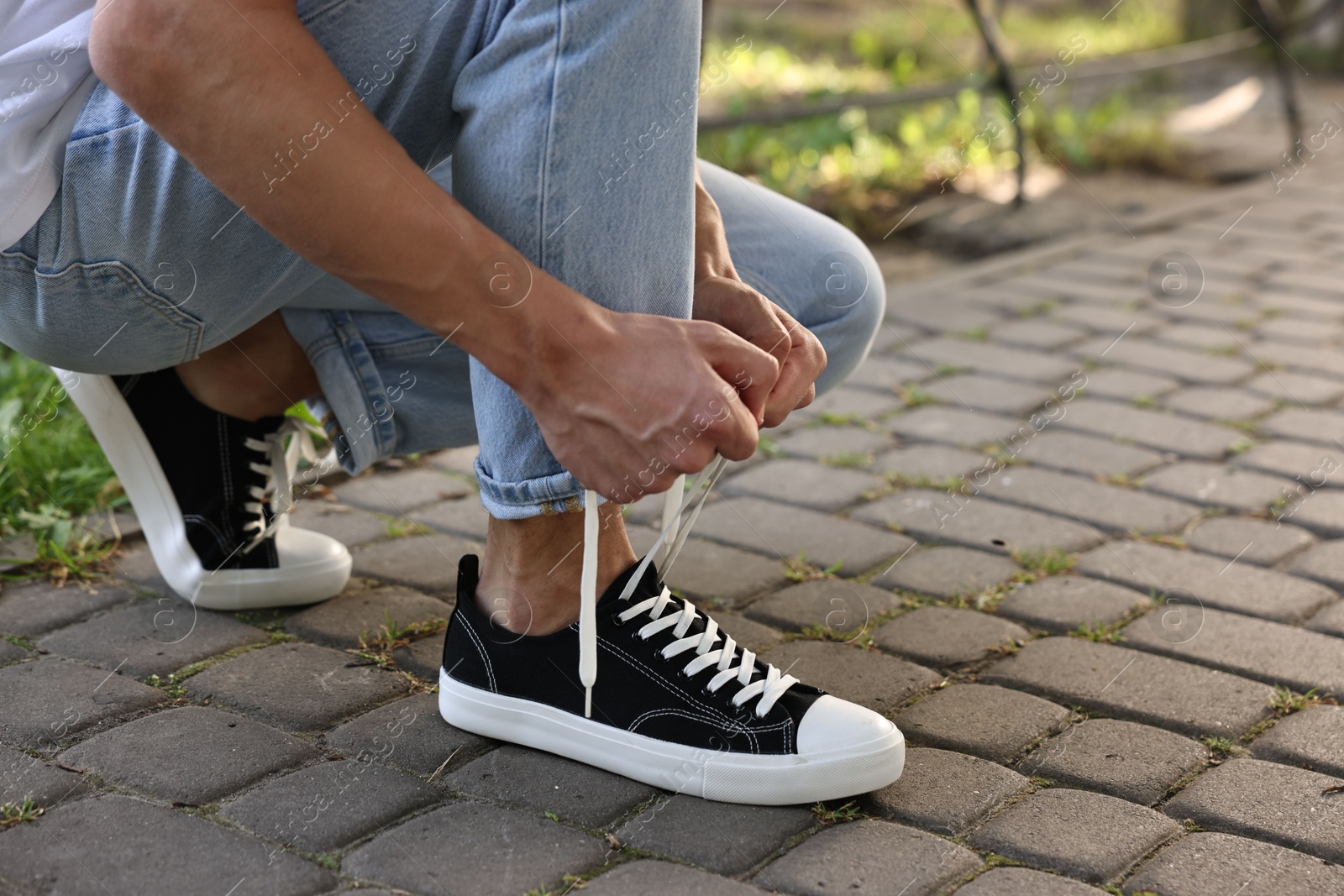 Photo of Man tying shoelace of black sneaker outdoors, closeup. Space for text