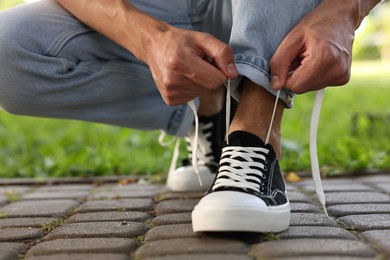 Photo of Man tying shoelace of black sneaker outdoors, closeup