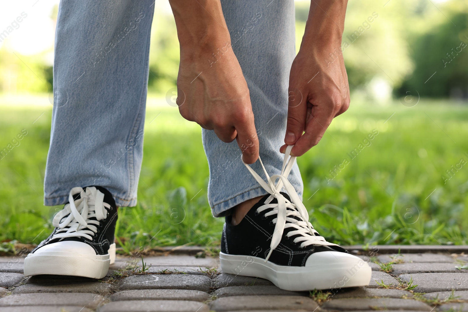 Photo of Man tying shoelace of black sneaker outdoors, closeup