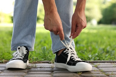 Photo of Man tying shoelace of black sneaker outdoors, closeup