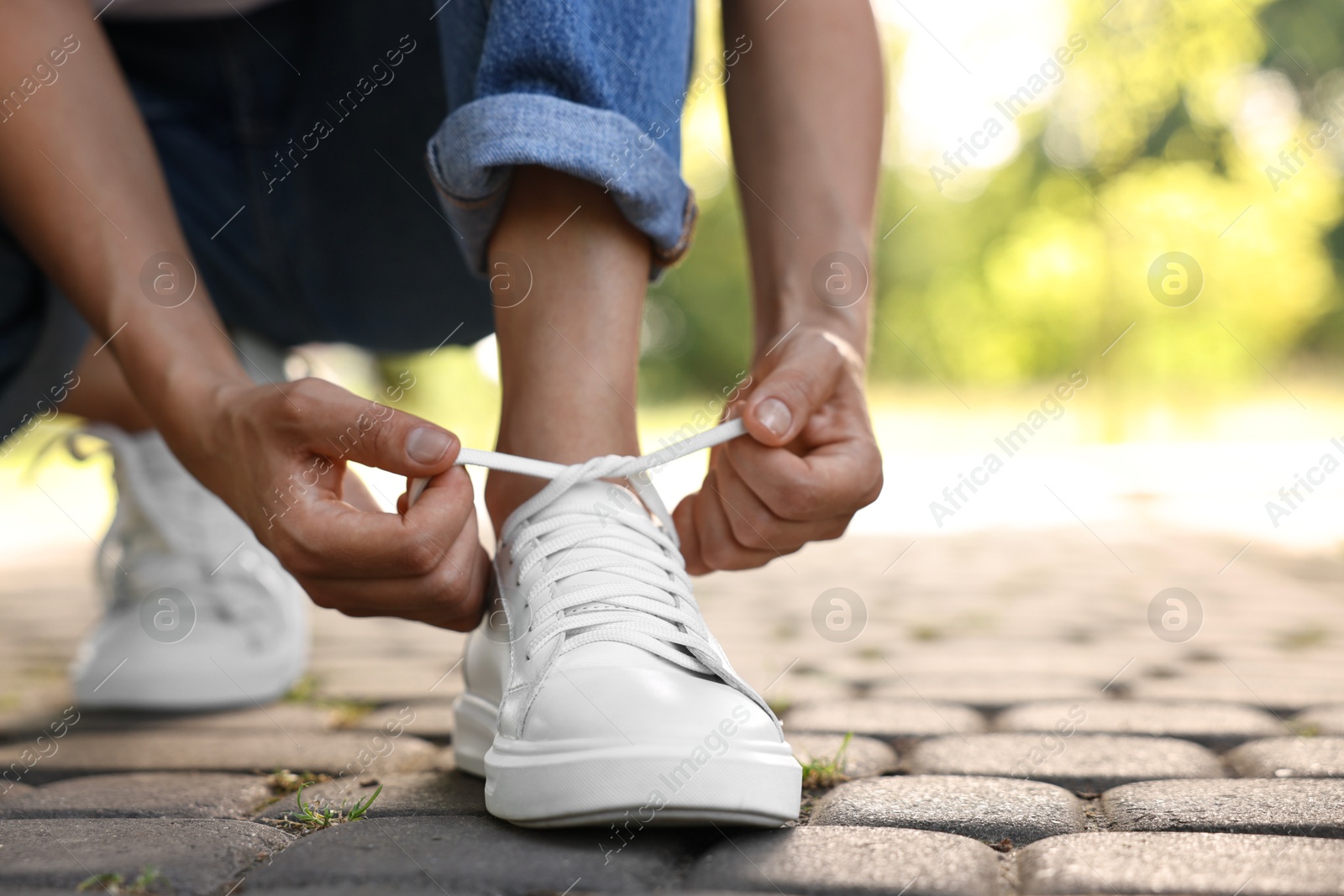 Photo of Woman tying shoelace of white sneaker outdoors, closeup. Space for text