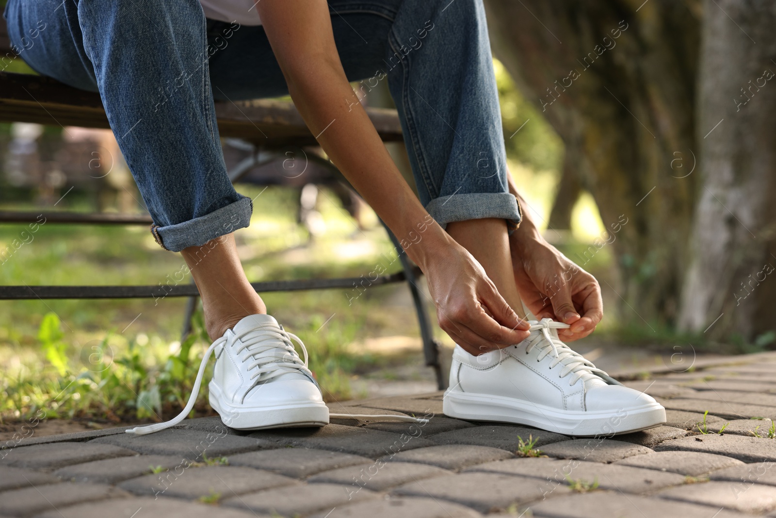 Photo of Woman tying shoelace of white sneaker outdoors, closeup