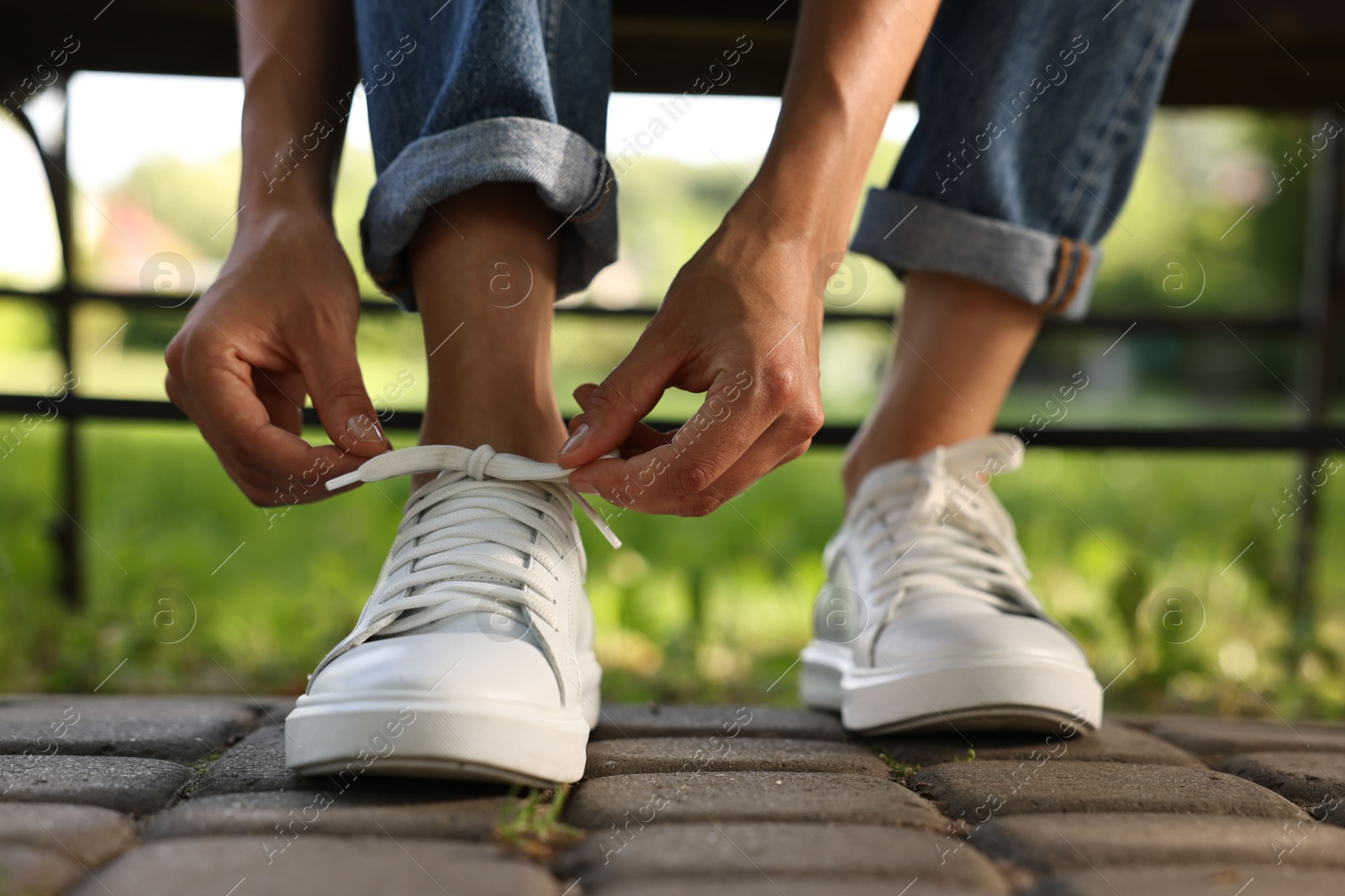 Photo of Woman tying shoelace of white sneaker outdoors, closeup