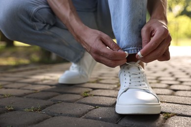 Photo of Man tying shoelace of white sneaker outdoors, closeup