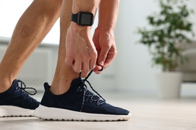 Man tying shoelace of sneaker indoors, closeup. Space for text