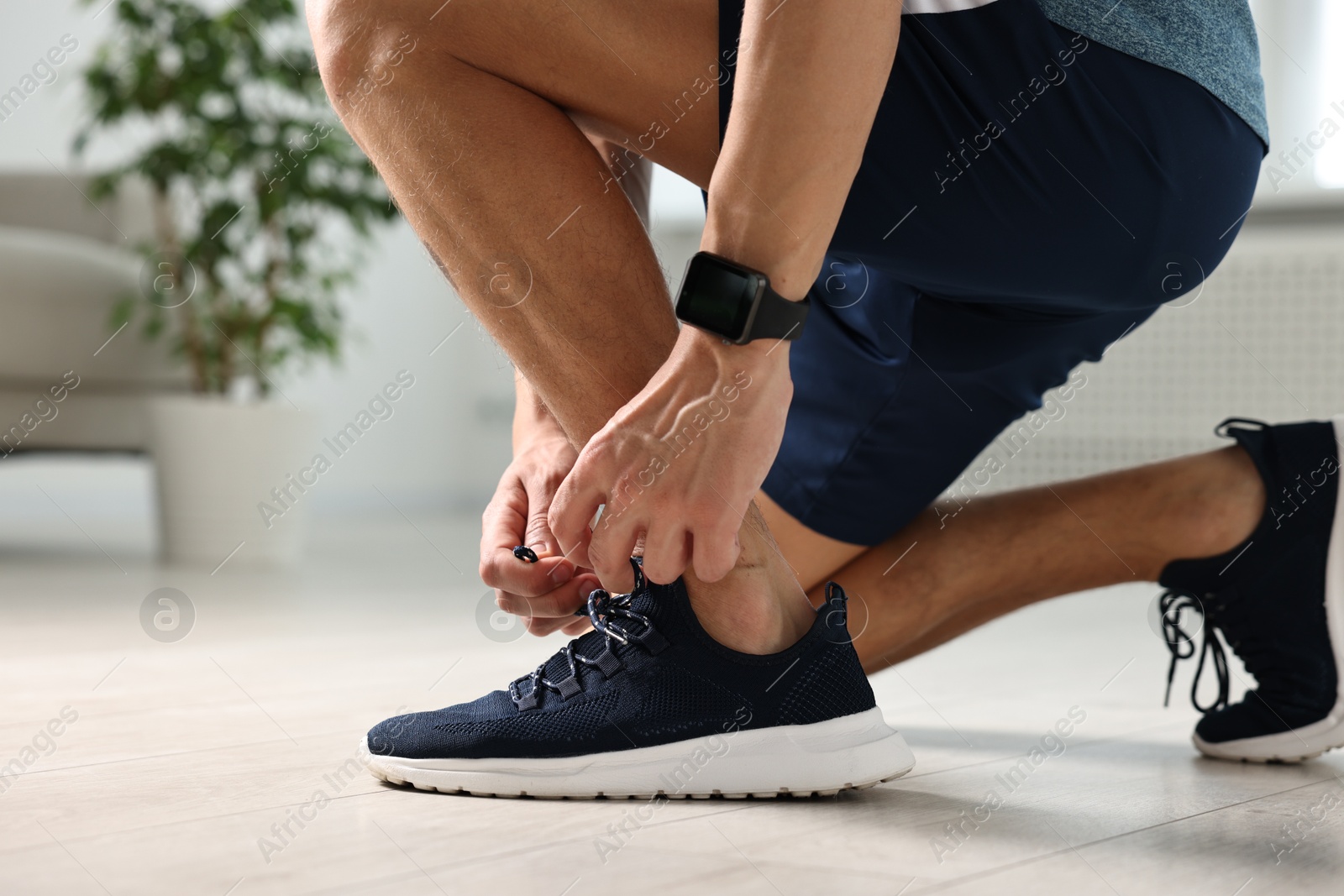 Photo of Man tying shoelace of sneaker indoors, closeup