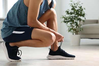 Photo of Man tying shoelace of sneaker indoors, closeup. Space for text