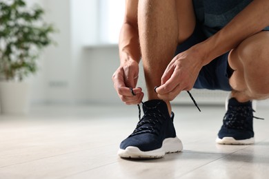 Photo of Man tying shoelace of sneaker indoors, closeup. Space for text