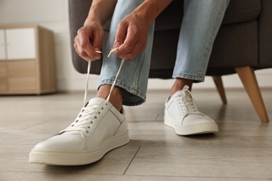 Photo of Man tying shoelace of sneaker indoors, closeup