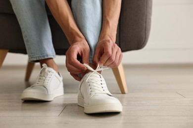 Photo of Man tying shoelace of sneaker indoors, closeup