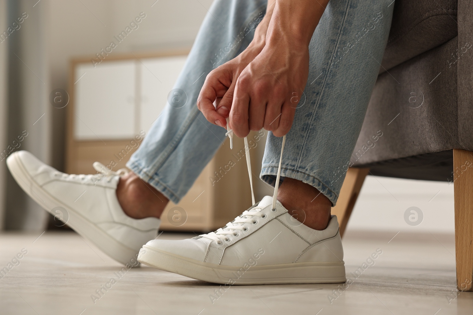 Photo of Man tying shoelace of sneaker indoors, closeup