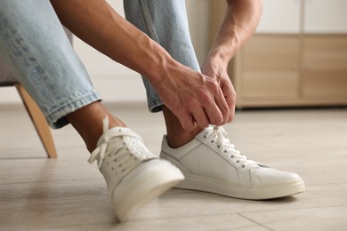 Photo of Man tying shoelace of sneaker indoors, closeup