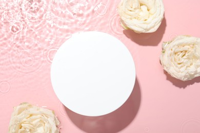 Beautiful rose flowers and round shaped podium in water on pink background, flat lay