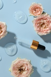 Photo of Beautiful rose flowers, pipette and drops of cosmetic serum on light blue background, flat lay