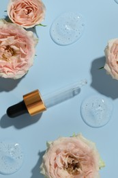 Photo of Beautiful rose flowers, pipette and drops of cosmetic serum on light blue background, flat lay