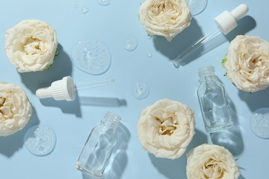 Photo of Beautiful rose flowers, cosmetic bottles, pipettes and drops of serum on light blue background, flat lay