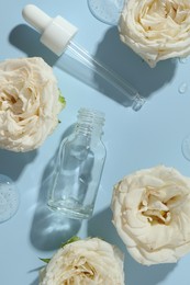 Photo of Beautiful rose flowers, cosmetic bottle, pipette and drops of serum on light blue background, flat lay