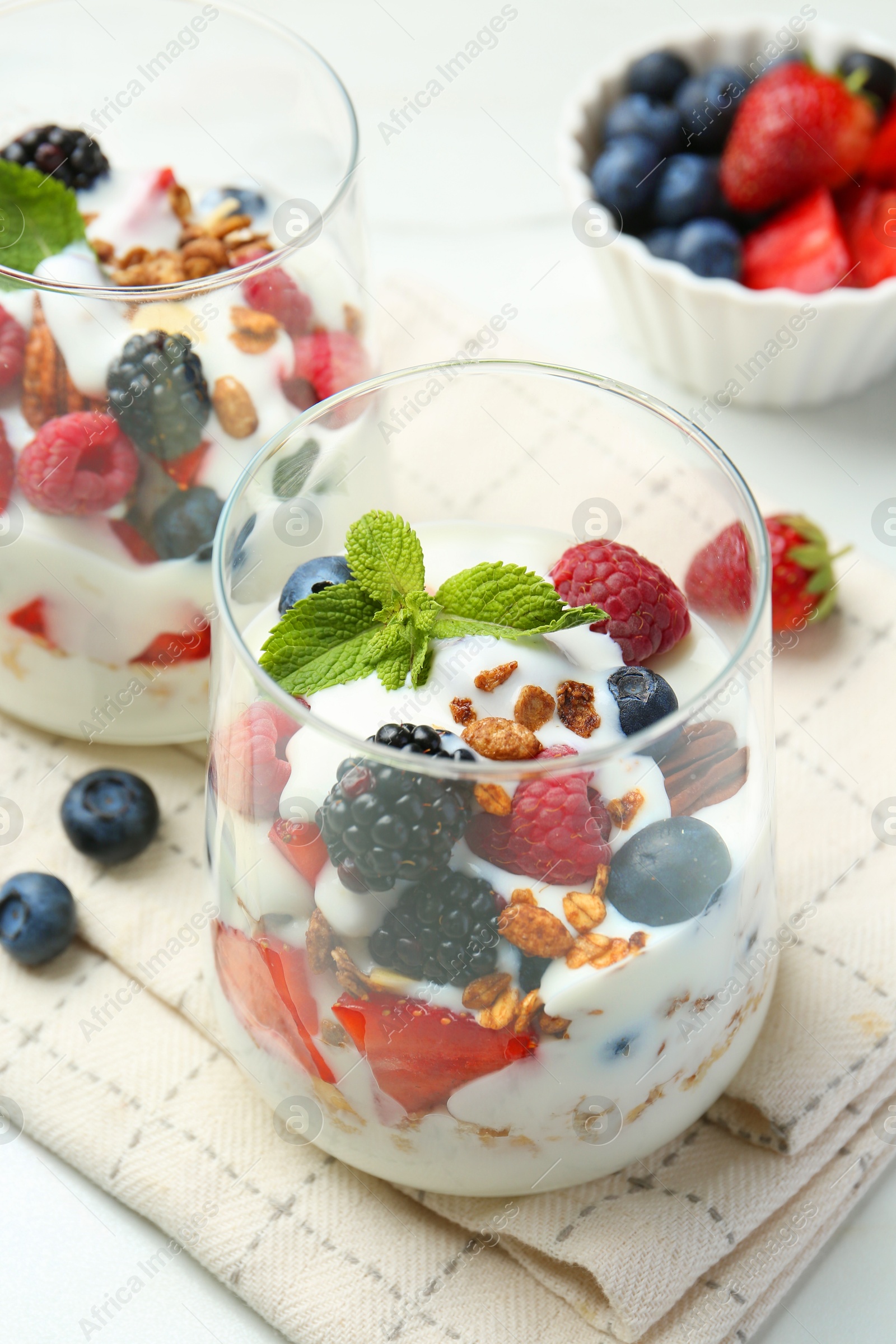 Photo of Tasty yogurt with fresh berries, granola and mint in glasses on table, closeup