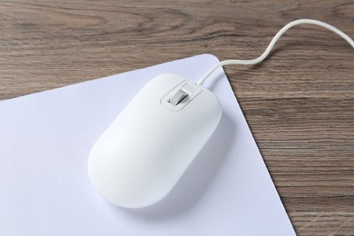 Photo of Computer mouse with mousepad on wooden desk, closeup