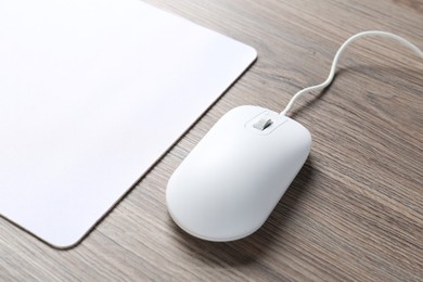 Photo of Computer mouse with mousepad on wooden desk, closeup