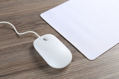 Photo of Computer mouse with mousepad on wooden desk, closeup