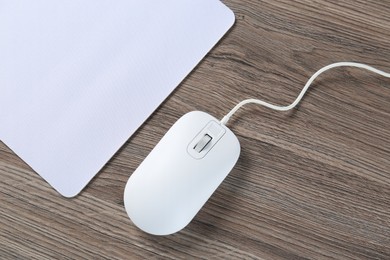 Photo of Computer mouse with mousepad on wooden desk, top view