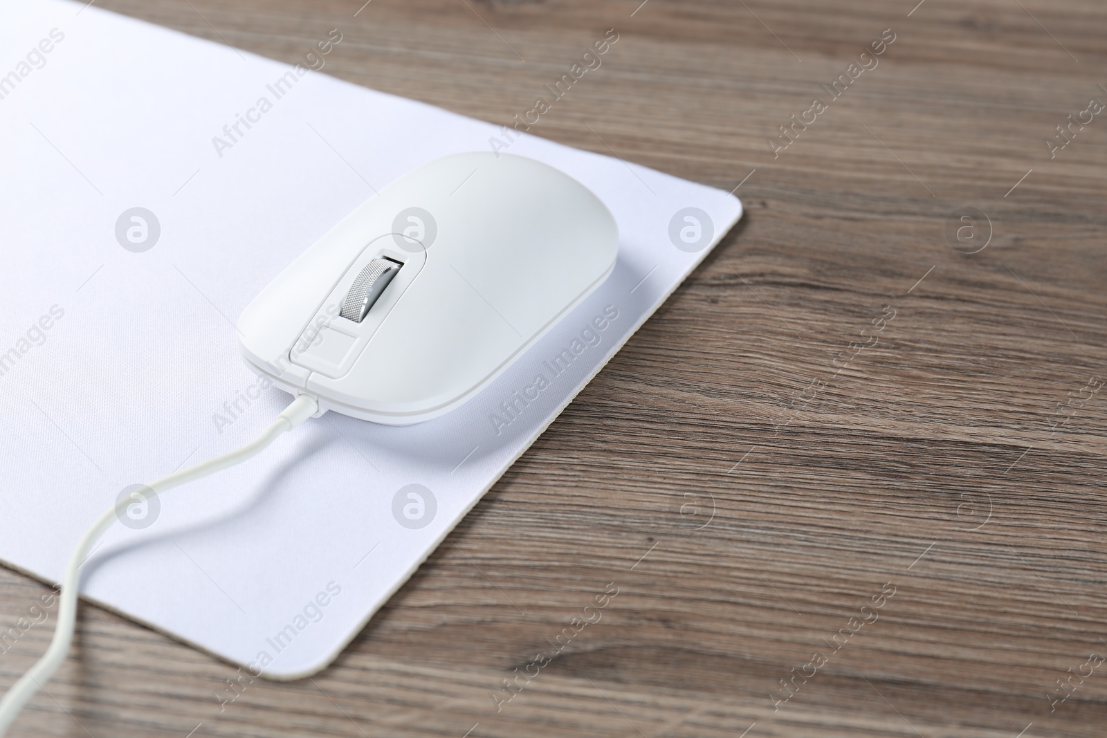 Photo of Computer mouse with mousepad on wooden desk, closeup