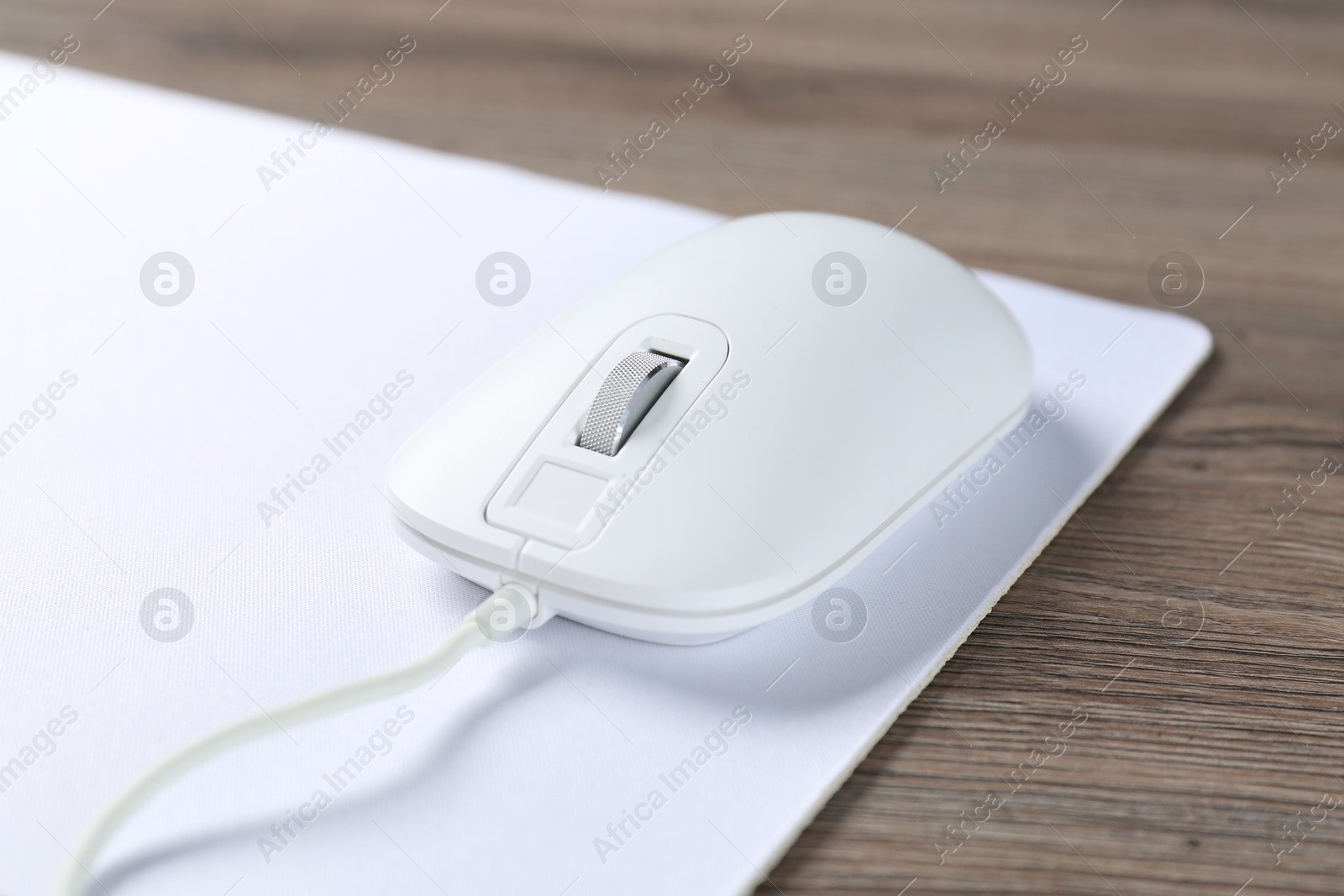 Photo of Computer mouse with mousepad on wooden desk, closeup