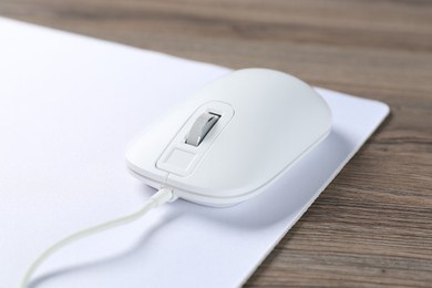 Photo of Computer mouse with mousepad on wooden desk, closeup