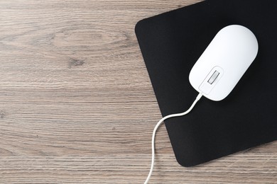 Photo of Computer mouse with mousepad on wooden desk, top view. Space for text