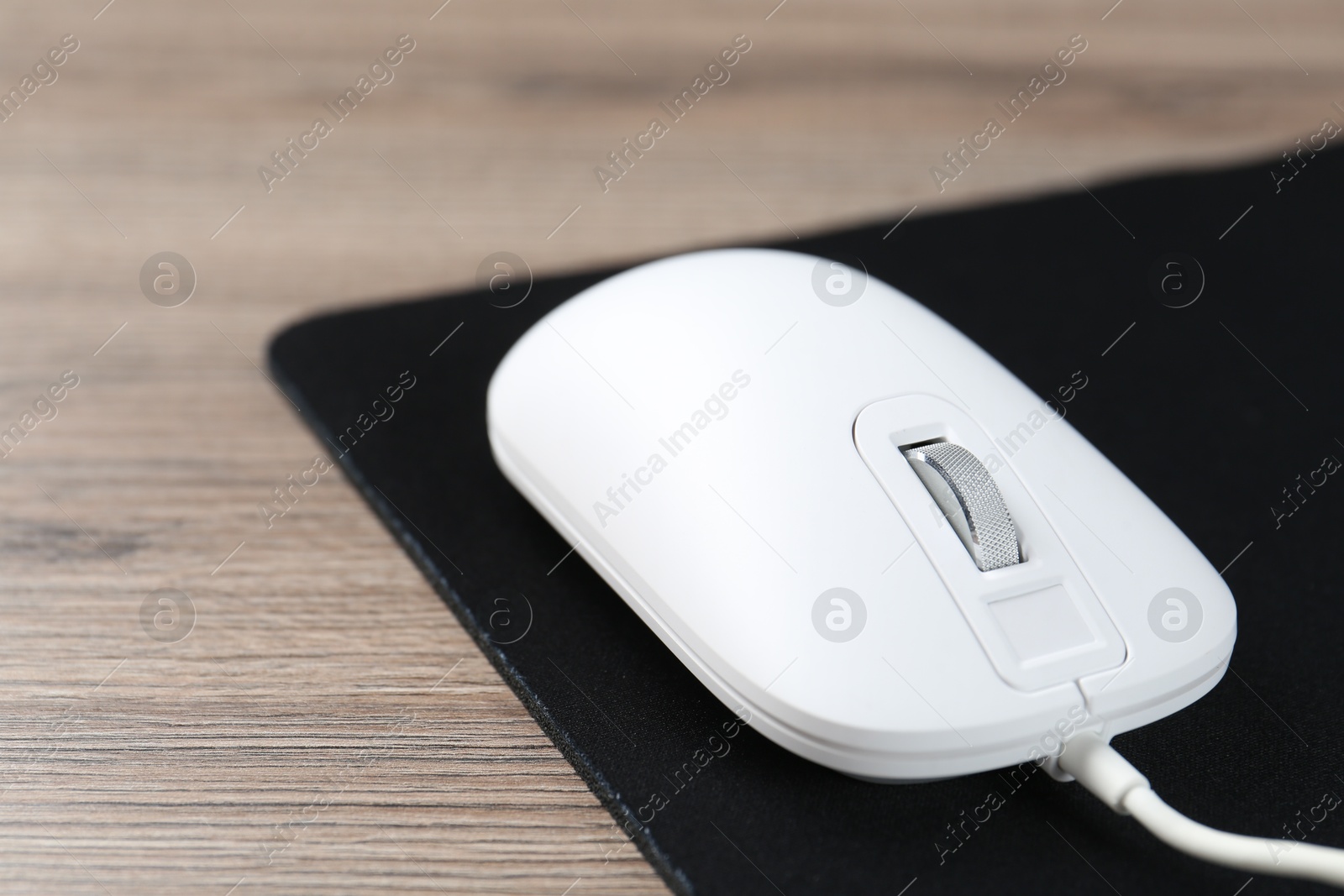 Photo of Computer mouse with mousepad on wooden desk, closeup