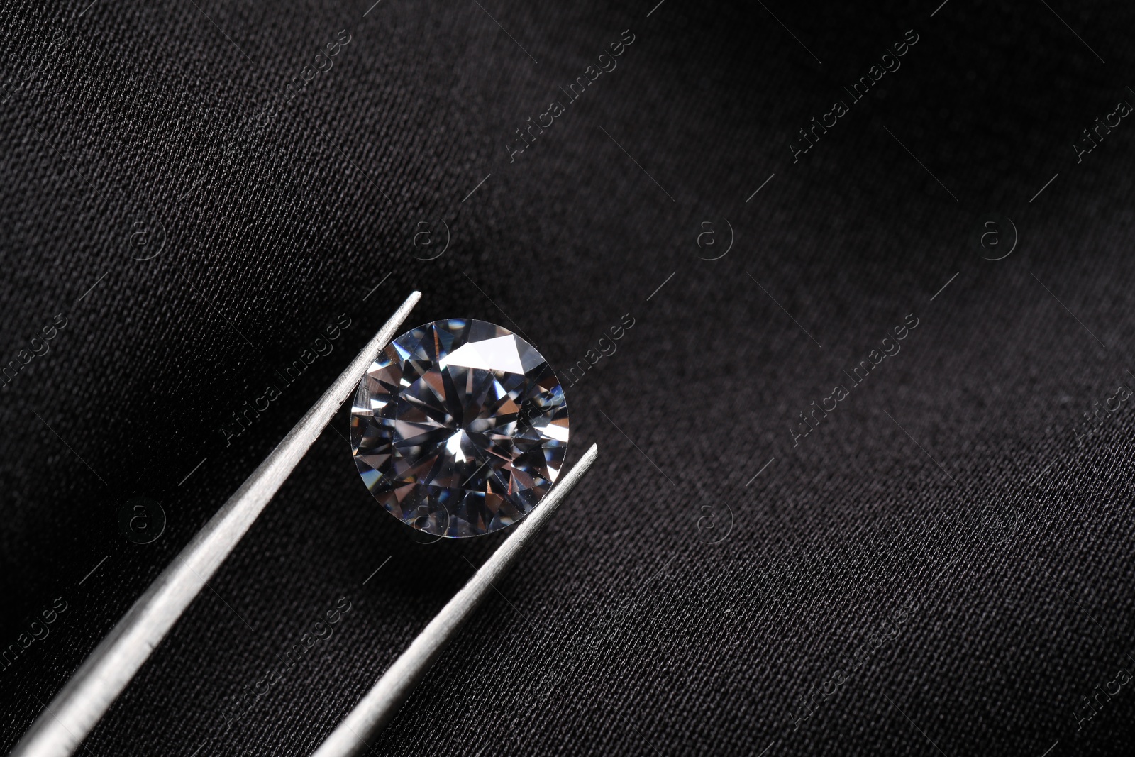 Photo of Tweezers with beautiful shiny diamond on black fabric, top view. Space for text