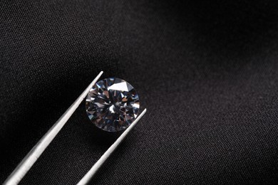 Photo of Tweezers with beautiful shiny diamond on black fabric, top view. Space for text