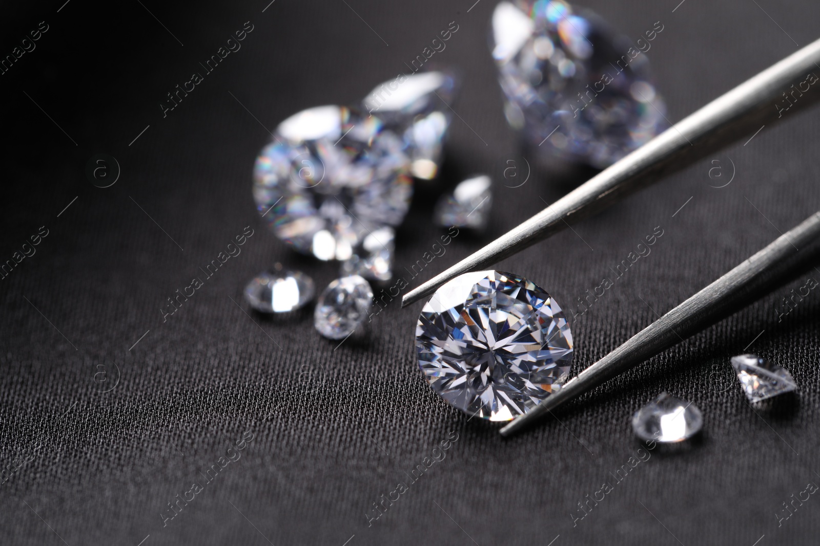 Photo of Tweezers with beautiful shiny diamonds on black fabric, closeup