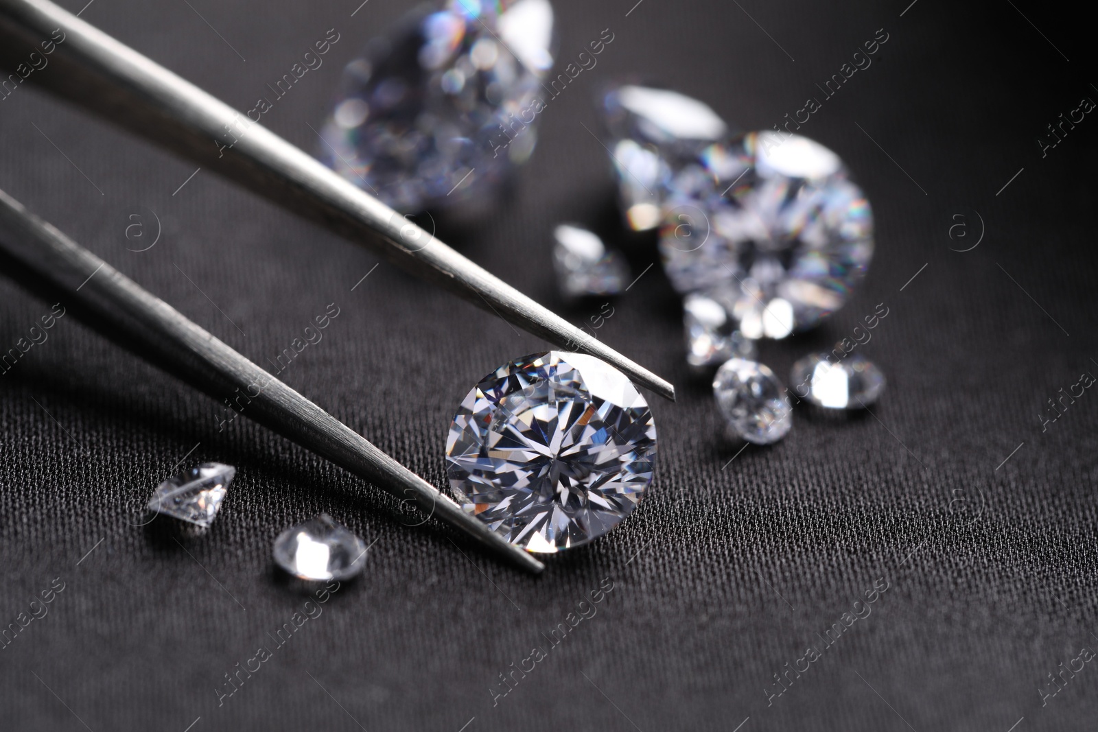 Photo of Tweezers with beautiful shiny diamonds on black fabric, closeup